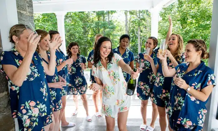 A bride opening a bottle of champaign while getting ready for her wedding with her bridesmaids