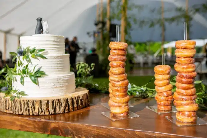 A wedding cake next to three towers of glazed donunts