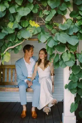 A couple holding hands on a porch bench and smiling