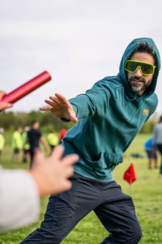 Man with sunglasses reaching for a baton to complete a leg of an obstacle race. Team building at Basin Harbor