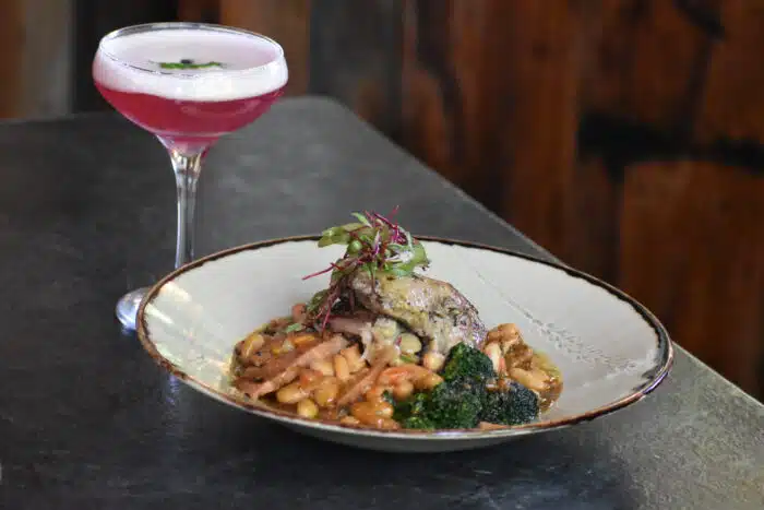 A close up of one of the chicken dishes served in Ardelia's on a grey countertop, next to a pink drink in a martini glass.